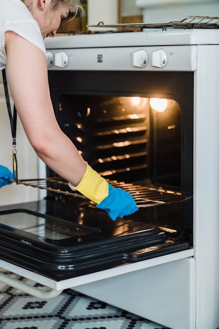 Close-up of a stainless steel oven with a digital control panel and an on/off button, situated in a modern kitchen. The oven door appears clean and shiny, reflecting light, while the adjacent kitchen 